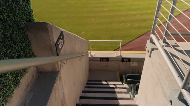 Steady forward glide down concrete stadium stairs toward outfield grass and seating section