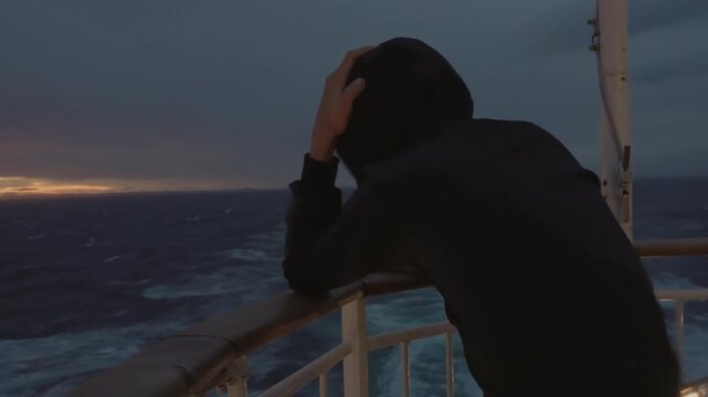 Boy in a hooded jacket on the aft deck, braving wind and waves on the ferry from Copenhagen to Oslo. An authentic, emotional moment during a rough weather sunset in Scandinavia.
