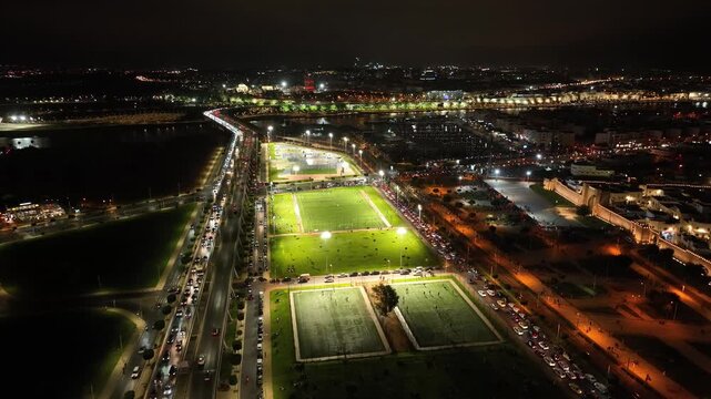 Aerial drone view of brightly lit sports fields in Rabat at night with surrounding roads, city lights and urban activity near the Bouregreg area in Morocco.