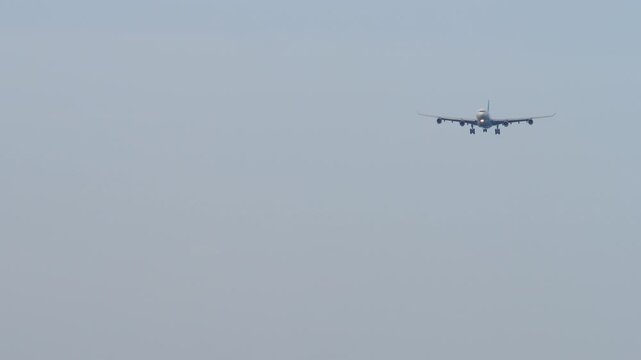 A huge four-engine aircraft with an unrecognizable livery approaching landing, front view long shot. Airplane in blue sky background. Travel concept