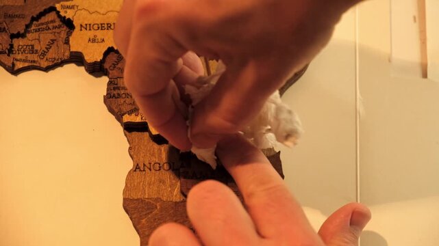 A man excess glue is wiped off with a paper napkin from a wooden world map of countries cutted out of plywood. The creative process of creating DIY crafts. Assembling a puzzle hobby. High quality 4K.