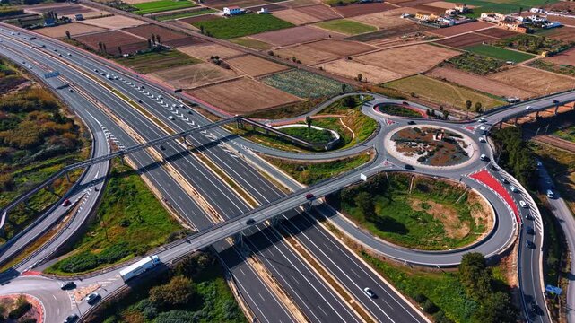 Flying to the lively highways with roundabouts and trestles. Intersection in the rural area with agricultural fields.