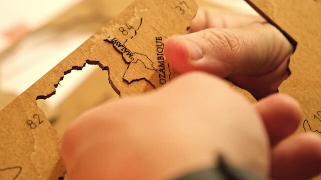 A man excess glue is wiped off with a paper napkin from a wooden world map of countries cutted out of plywood. The creative process of creating DIY crafts. Assembling a puzzle hobby. High quality 4K.