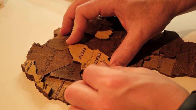 An unrecognizable man glues a wooden world map of countries cut out of plywood. The creative process of creating DIY crafts from above. Assembling a puzzle. Hobby concept. High quality 4K footage.