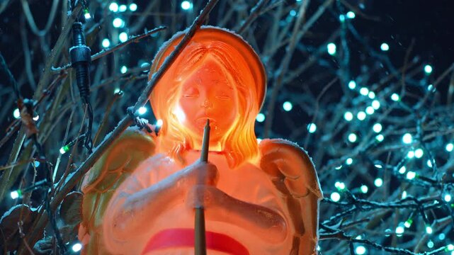 Figure of angel under the falling snow. Christmas d&eacute;cor among the tree branches and light garlands.