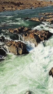 Aerial view of powerful rapids and rocky terrain at Khone Falls, Laos, with clear turquoise water rushing over rugged stones. Dramatic natural landscape ideal for travel and nature concepts.