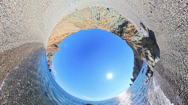 Beach ocean panorama showing a rocky coastline and clear blue sky from a tiny planet perspective during a sunny day