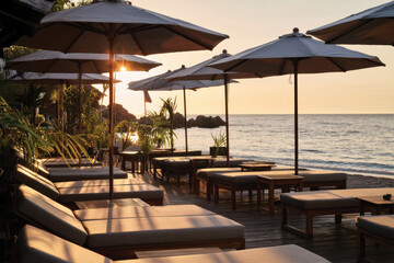 Fototapeta premium A scenic view of lounge chairs under sunlit umbrellas along the beach, inviting relaxation and comfort while enjoying the soothing sounds of the ocean waves.