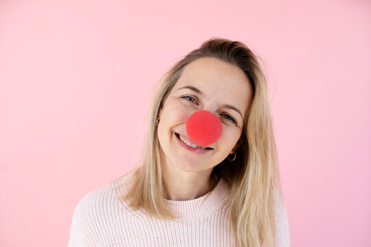 blond woman in front of pink background with red clown nose