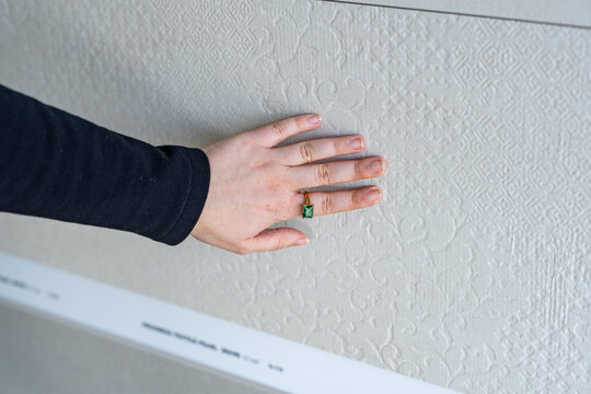 Main portant une bague verte touchant un mur blanc, cr&eacute;ant une sc&egrave;ne minimaliste mettant en valeur le contraste entre la peau, l&rsquo;accessoire et la surface murale.