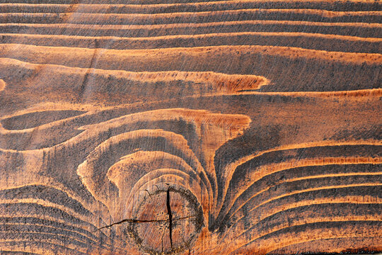 Close up of a dark stained pine wood surface showing natural grain patterns and a prominent circular knot in the center