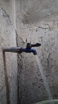 Footage of water flowing from a blue plastic faucet on a rough concrete wall background for domestic hygiene and water conservation concept