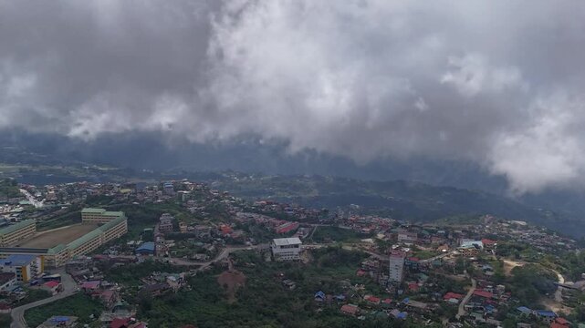 Aerial hyperlapse of fast-moving clouds rolling over the dense, mountainous residential cityscape of Baguio City, Philippines