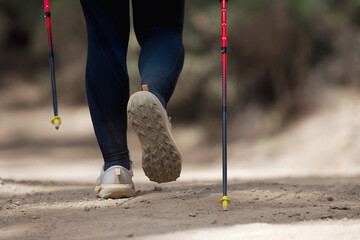 Senior woman walking in forest with Nordic walking sticks, sunny summer day. An active lifestyle in retirement, a hike in nature