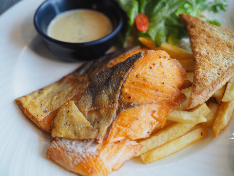 Salmon steak and vegetable salad, french fries, are served on the plate. It looks appetizing and tastes delicious.