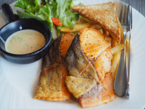 Salmon steak and vegetable salad, french fries, are served on the plate. It looks appetizing and tastes delicious.