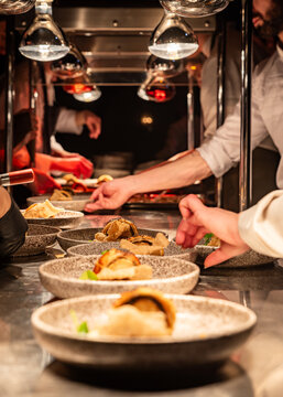 A busy kitchen service area with lots of chefs hands and dishes being prepared for serving to guests