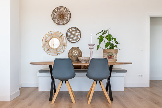 A wooden dining room table with two grey chairs, a plant and various beach themed wall and table decorations in a home lounge with a white wall.