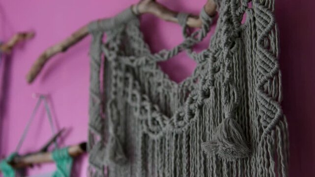 Handmade macrame wall decor on pink rural house wall with traditional woven patterns creating cozy boho atmosphere and authentic countryside interior style
