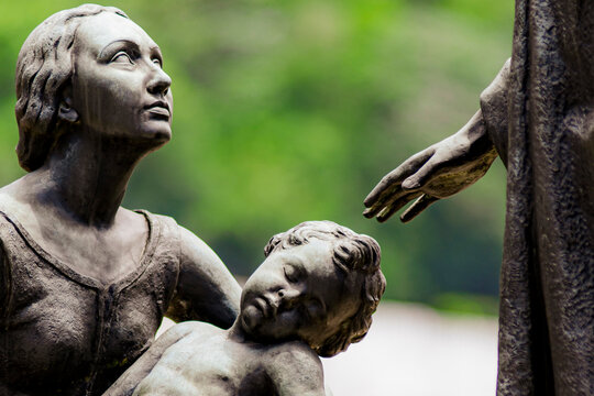 Statue depicting a mother kneeling with her sleeping child in her arms.Her gaze is pleading and directed towards an outstretched hand symbolizing Jesus.Artist unknown,S&atilde;o Jo&atilde;o Batista Cemetery,RJ,BR.
