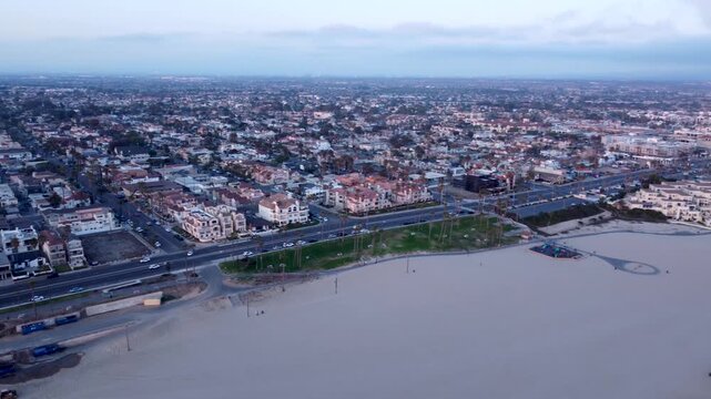 Huntington Beach Looking South towards Newport and Laguna at Sunset. Cars Drive by Tropical Palm Trees at Sunset. Warm golden hour light and calm Ocean waves. Orange County, California.