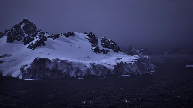 dusk framed remote ice escarpment rising from rough sea, jagged rock peaks and heavy snowfields emphasize scale, isolation, and raw geological detail suitable