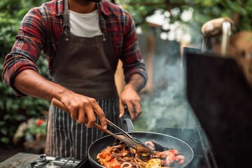 Fototapeta premium Male cook stir frying seafood in skillet at backyard grill station