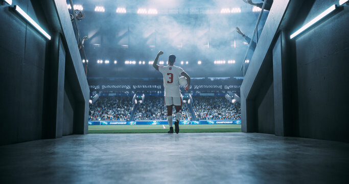 White Male Soccer Player Carries the Match Game Ball From the Tunnel Onto the Pitch, Saluting Supporters Before an International Championship Game in a Packed Stadium, World LEague Cup Event.