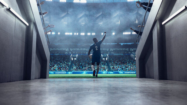 Black Male Soccer Player Runs From the Tunnel Onto the Pitch With Ball in Hand, Raising His Arm to Supporters Before a Professional International Football Match Game in a Packed World Euro Stadium.