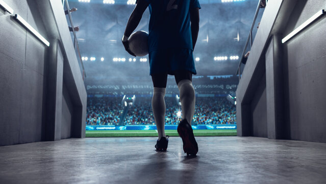 Black Male Soccer Player Walks From the Stadium Tunnel Onto the Pitch Holding the Ball Before a Professional International Football Match, With a Full Arena Set for a Major World Euro Tournament.