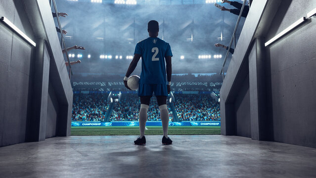 Black Male Soccer Player Stands at the Tunnel Entrance Holding the Ball, Facing a Packed Stadium Before Kickoff in a Professional International Football Euro and World Tournament Scene.