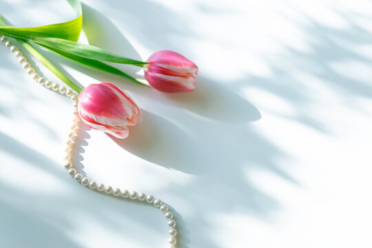Pink tulips with pearl necklace on white background, elegant spring flat lay with copy space