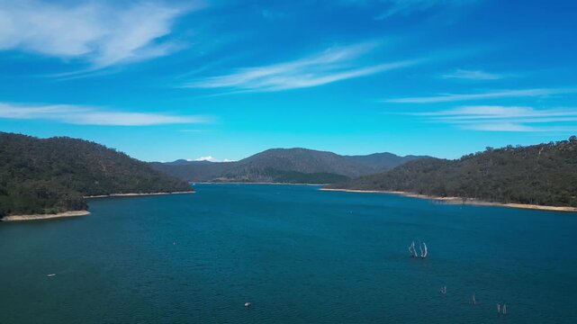 Drone flying over Lake Eildon in Victoria, Australia with blue water and green hills and mountains. Aerial view of calm lake landscape in daylight, suitable for travel and nature concepts.