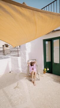 Woman relaxing on a sunlit terrace in southern Italy. Mediterranean architecture, white stone walls, soft summer light and quiet slow living atmosphere. Calm everyday life and peaceful southern