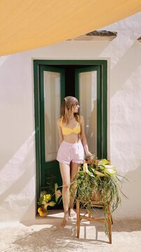 Static video of a woman opening the door and stepping onto her terrace in southern Italy. Mediterranean summer light, fresh air, calm everyday moment and peaceful slow living lifestyle atmosphere