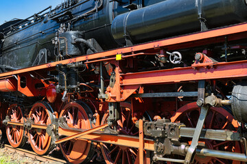 Fototapeta premium Detailed view of a vintage steam locomotive undercarriage with red wheels and mechanical parts