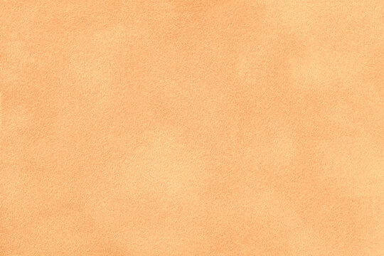 Light peach suede fabric background with matte nap velvet texture. Pastel orange soft felt textile surface in macro