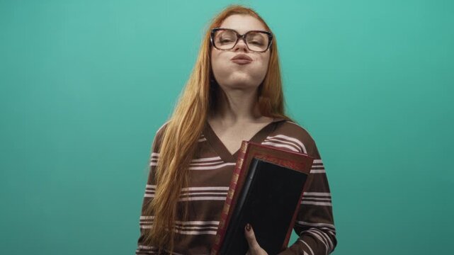 Redhead woman in striped brown sweater holding ornate hardcover book with lips pursed and oversized glasses in a studio; playfulness.