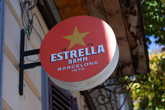 Tbilisi, Georgia - September 23, 2025: Horizontal street city photo. Red board sign with logo of Spanish beer brand Estrella Damm, golden star on bar brick wall or entrance to alcoholic cafe