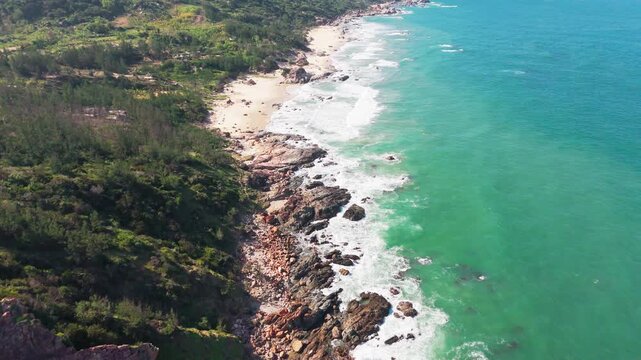 Cinematic Aerial Drone View of Lush Forested Hillside Meeting Rocky Emerald Coastline at Bai Bang, Quy Nhon, Binh Dinh Province, Central Vietnam, Southeast Asia