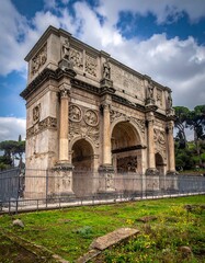 Obraz premium A grand ancient stone archway stands under a cloudy sky. Trees and grass surround it