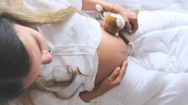 Expectant mother sitting in bed with baby shoes, getting ready for the new arrival