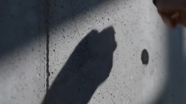 Close-Up of a Hand Inserting a Small Black Object Into a Hole in a Concrete Wall