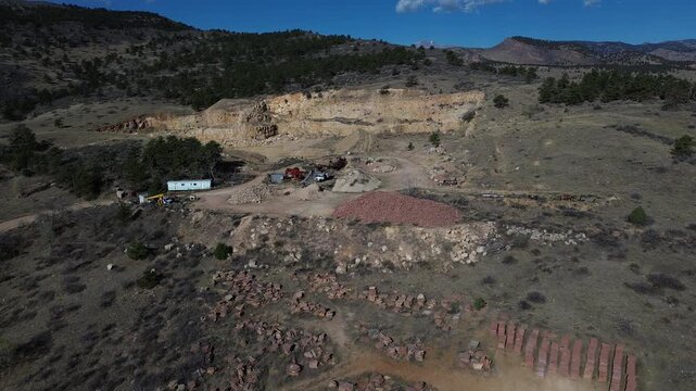 Foothill quarry cut near N Foothills Hwy by Hygiene showing exposed rock faces and equipment positioned along carved benches beside open rangeland. Sharp edges, coarse debris in Longmont, CO