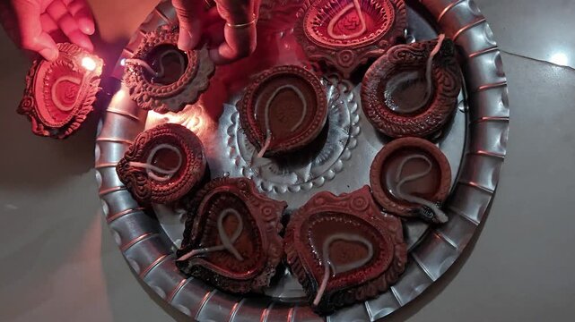 A festive moment of lighting diyas, which are traditional oil lamps made from clay used during Hindu, Jain, and Buddhist celebrations, such as Diwali. Lighting unlit diyas by lit diya holding in hands