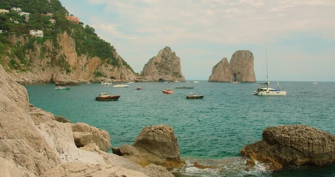 Many luxury yachts and small boats float on calm sea by Faraglioni rocks in Capri Island Italy