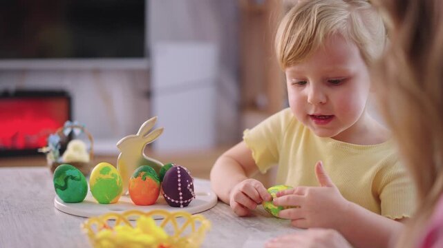 Child paints Easter eggs with care and focus. Soft light warms the cozy, festive setting. Parent's hand guides the child's small fingers. Bright colors match springtime joy and creativity