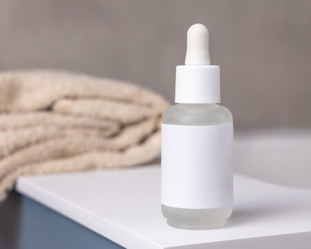 Dropper bottle with blank label near bath towels in beige bathroom, cosmetic mockup