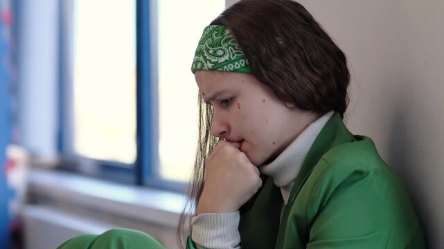 A troubled young woman leans against the wall, her expression filled with frustration and emotional struggle. The image conveys the weight of perfectionism, societal expectations, and the unseen