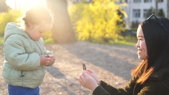 Mother and daughter in the park on a sunny spring day, playing with twigs